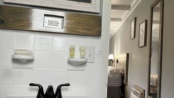 A bathroom with a white sink, a mirror, and a shower area. There are toiletries on the wall and a towel rack.