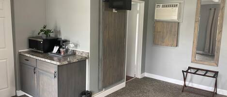 A kitchen with a granite countertop, a microwave, and a small plant. There is a wooden door and a white door.