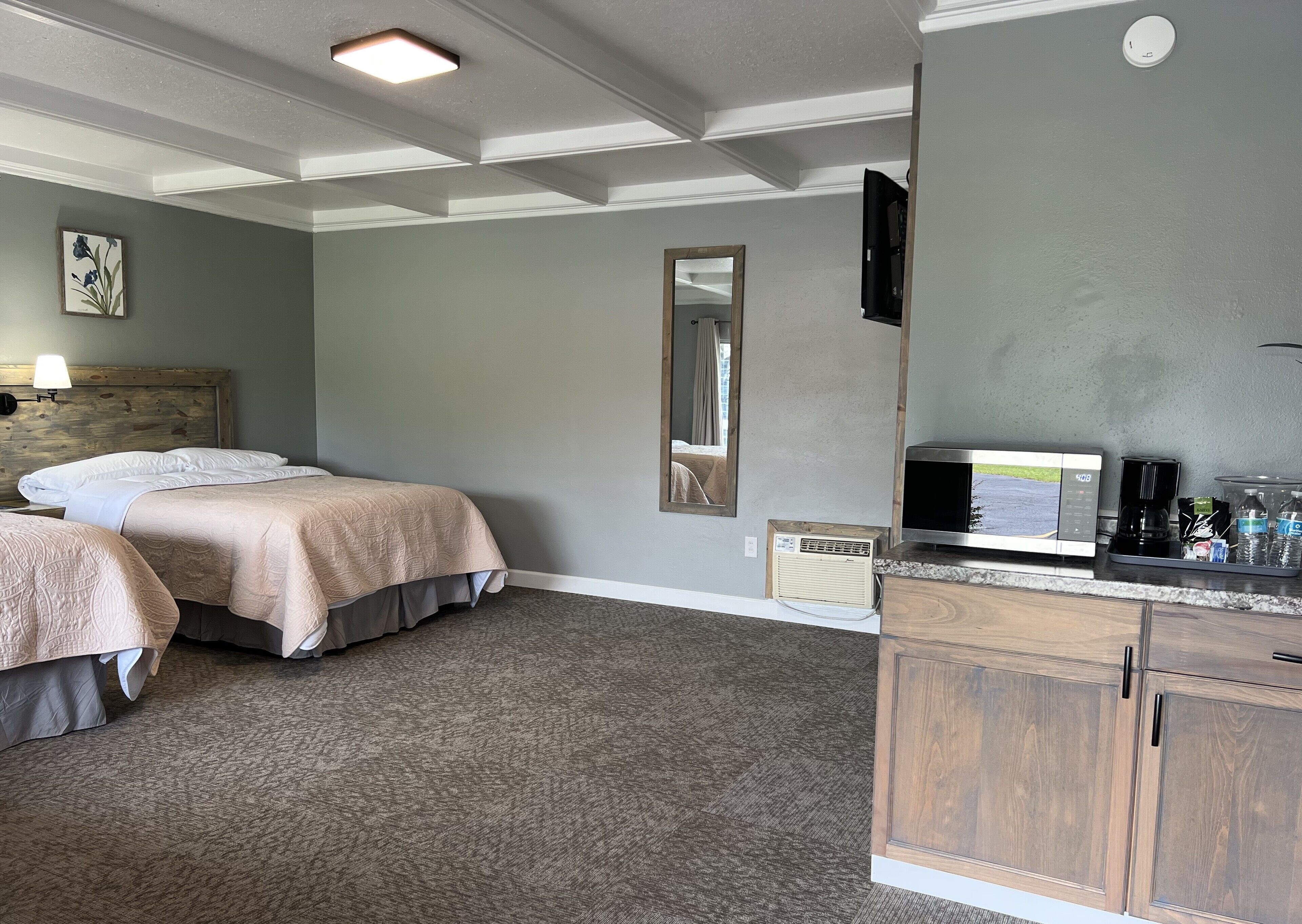 Ein Hotelzimmer mit zwei Betten, einem großen Spiegel, einem Flachbildfernseher, einer Kaffeemaschine und einem Wasserspender.