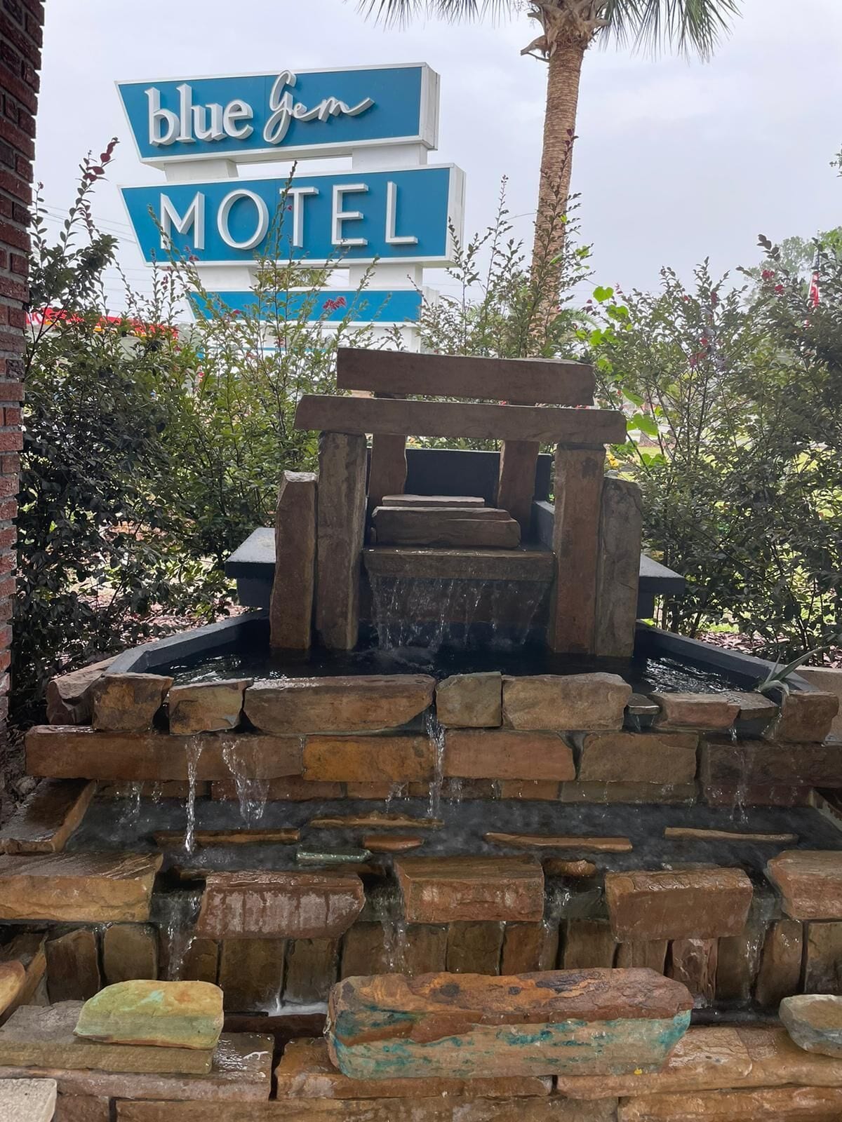 A Blue Gem Motel sign above a stone water feature with a wooden bench.