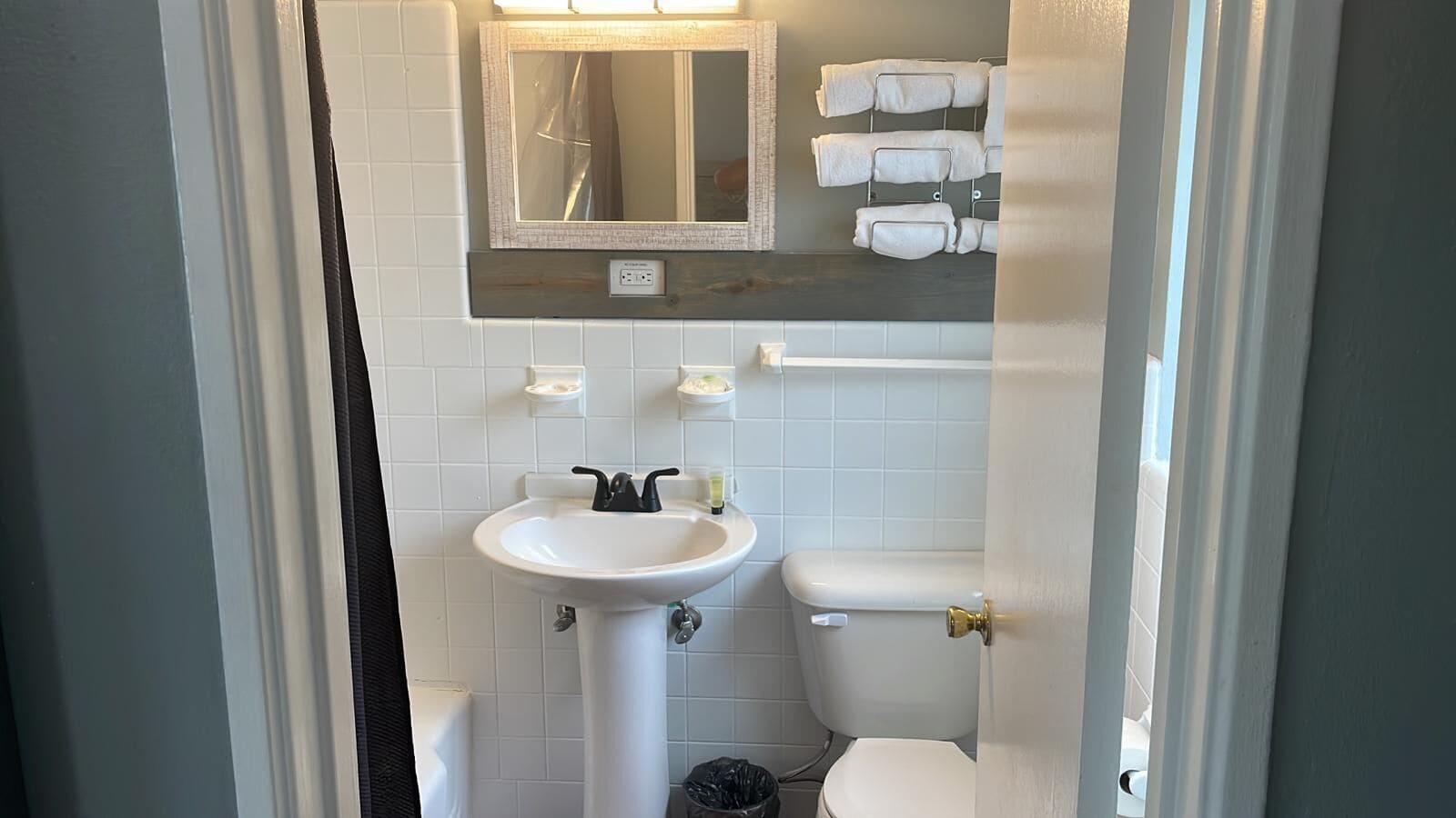 A bathroom with a white sink, a toilet, and a mirror above the sink. There are towels hanging on a rack above the toilet.