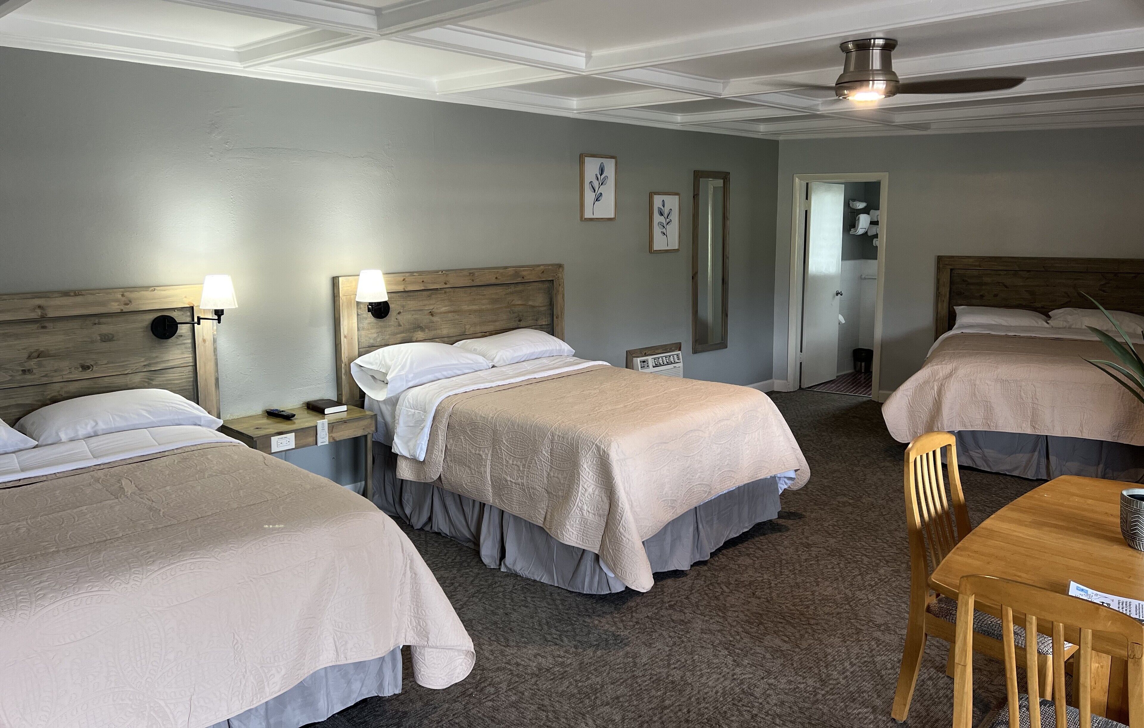 A hotel room with two beds, a wooden headboard, bedside lamps, a small table, and a chair.