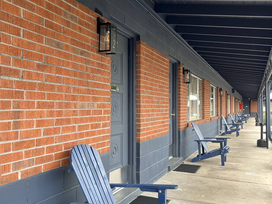 A row of blue Adirondack chairs along a covered walkway with brick walls and doors.