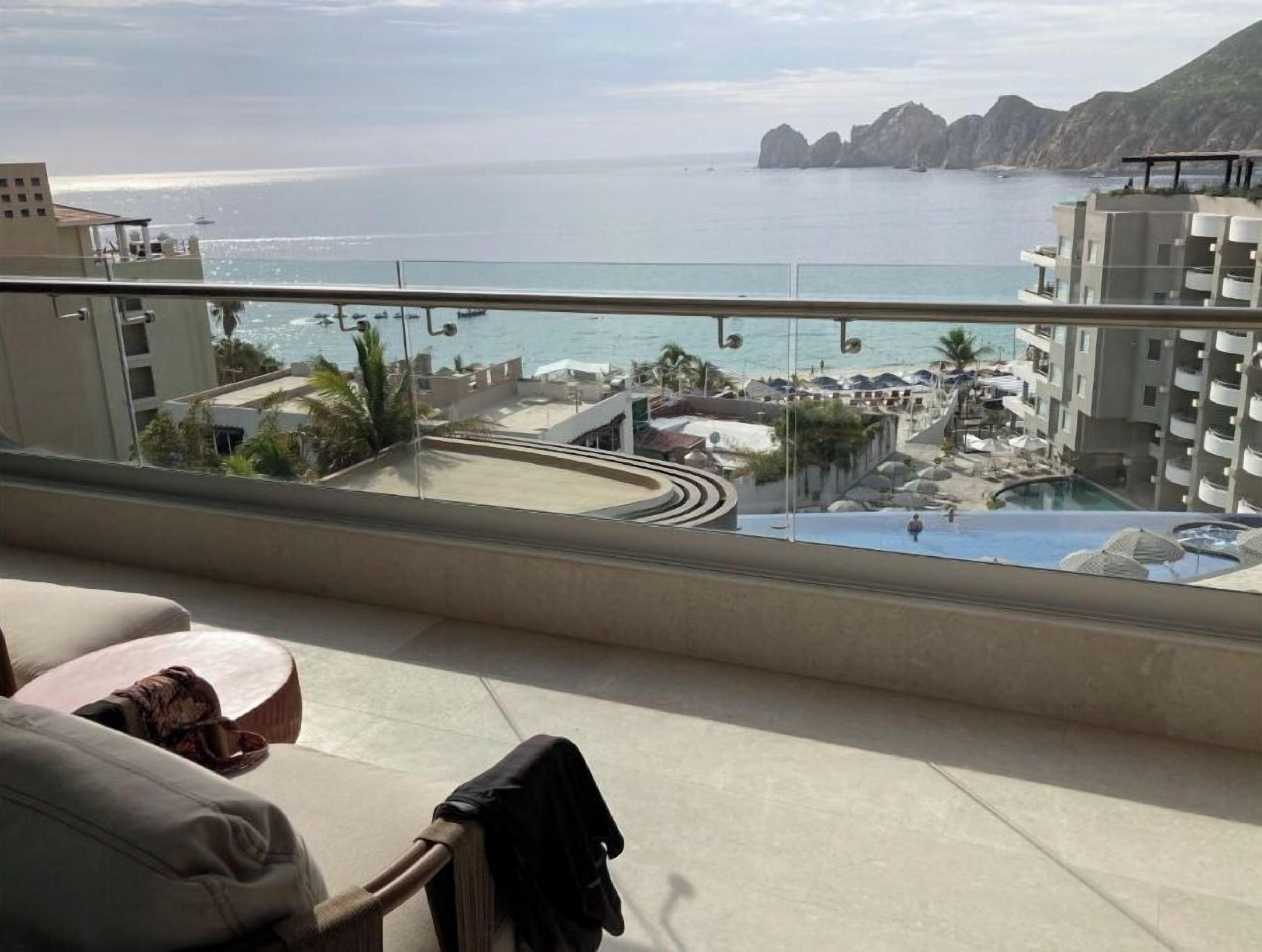 Un balcón con vistas a un resort en la playa, que incluye una piscina y zona de descanso.