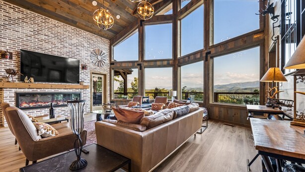 Un salon spacieux doté d’une cheminée, d’un canapé en cuir et de grandes fenêtres offrant une vue sur les montagnes.