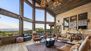Un salon spacieux doté de grandes fenêtres, d’une cheminée et offrant une vue sur les montagnes.