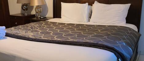 Una cama bien hecha con una colcha estampada, un cabecero de madera y dos lámparas de noche.