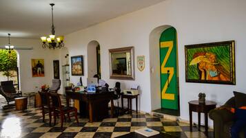 A hotel lobby with a checkered floor, a reception desk, several chairs, a chandelier, and artwork on the walls.