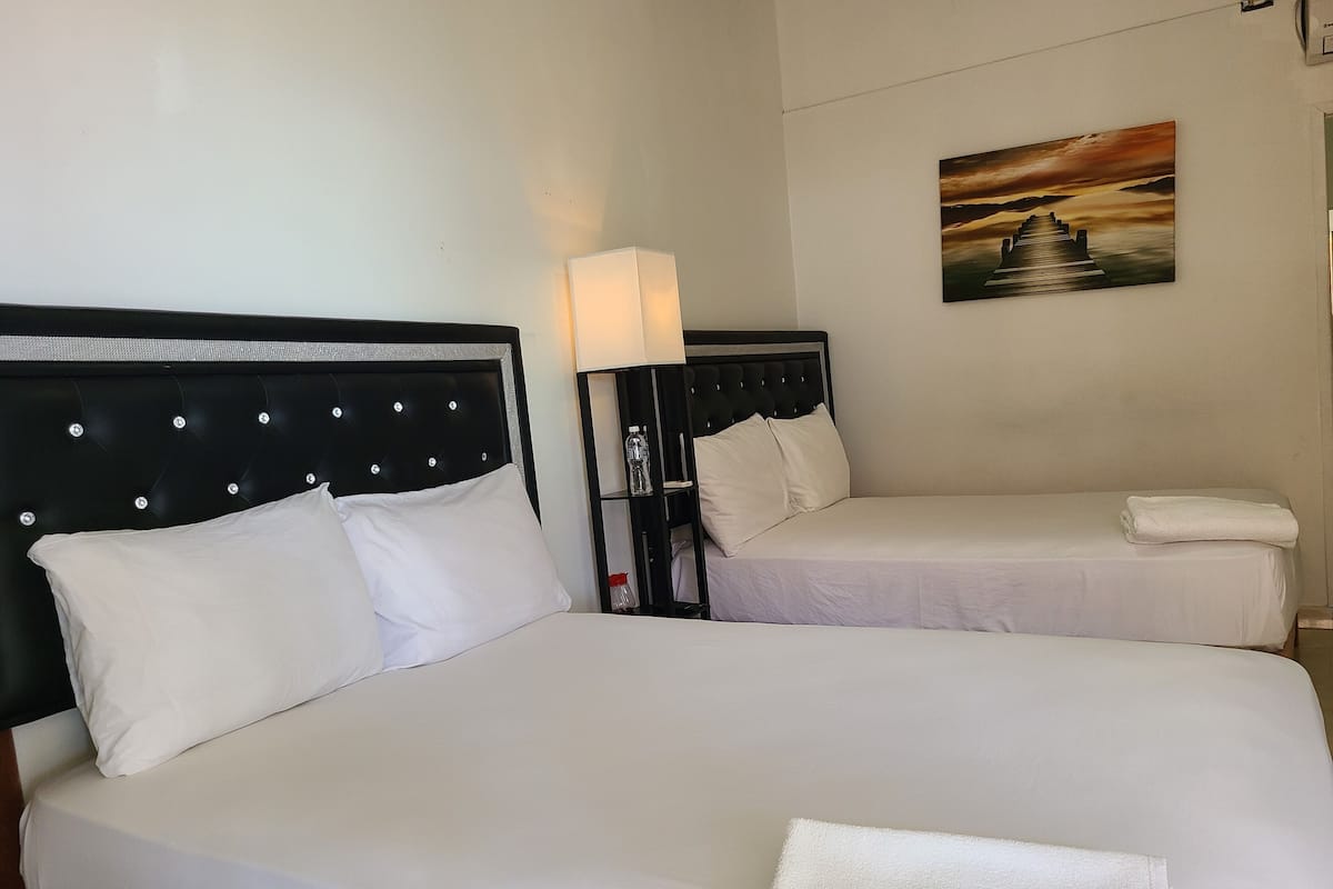 A hotel room with a large bed, a smaller bed, a nightstand with a lamp, and a painting on the wall.