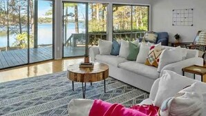 A modern living room with a white sofa, a round coffee table, and a view of a lake through large glass doors. - Your Private Lakefront Retreat (Nacogdoches)
