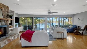 A spacious living room with a fireplace, white sofas, and a large window overlooking a scenic view. - Your Private Lakefront Retreat (Nacogdoches)