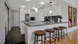 A modern kitchen with a central island, bar stools, and pendant lighting. - Your Private Lakefront Retreat (Nacogdoches)
