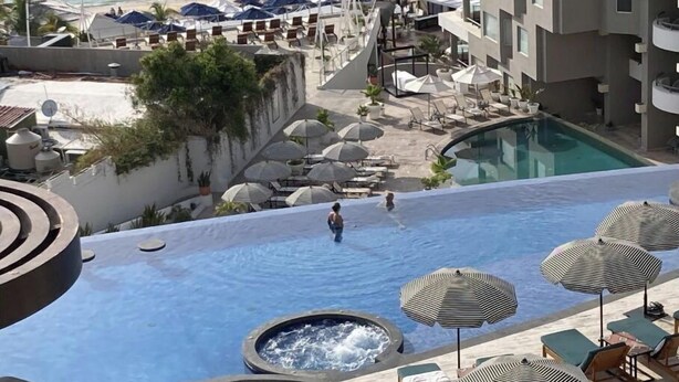 A rooftop infinity pool with lounge chairs and umbrellas, overlooking a beach. - Sunset Suite (Cabo San Lucas)