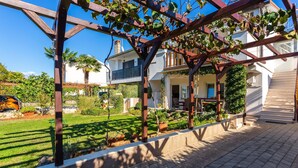 Ein Wohnhaus mit überdachter Terrasse, Garten und zweistöckigem Gebäude.