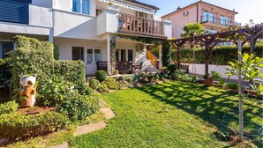 Ein zweigeschossiges Haus mit einer überdachten Terrasse, einem kleinen Garten und einer Holzw pergola.