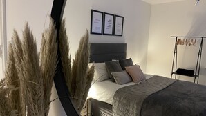 A bedroom with a bed, pillows, a bedside table, a wall-mounted shelf, and a mirror. - Luxury hotel style 2-bed home with hot tub central location (pet friendly) (Wooler)