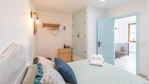 A bedroom with a bed, a dresser, a wall-mounted light, and a door leading to a balcony. - Casa La Botica Frigiliana by Ruralidays (Málaga)