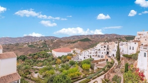 Une ville perchée sur une colline, avec des bâtiments blancs, des jardins en terrasses et un ciel d’un bleu limpide.