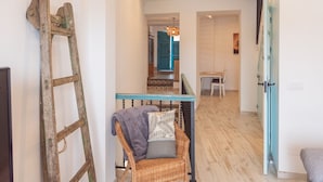 Un couloir avec un fauteuil en osier, une échelle en bois et un escalier menant à une autre pièce.
