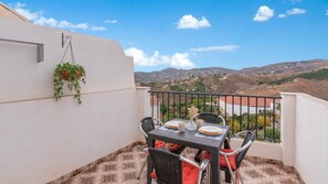 A balcony with a table set for two, chairs, and a hanging plant. - Casa La Botica Frigiliana by Ruralidays (Málaga)