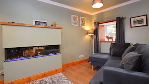 Een woonkamer met een open haard, een bank, een lamp en een raam met gordijnen.