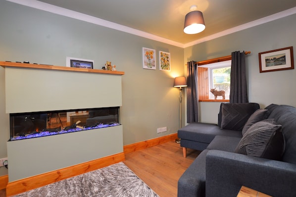 Un salon avec une cheminée, un canapé, une lampe et une fenêtre avec des rideaux.