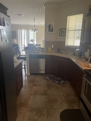 A kitchen with a built-in dishwasher, a dining area with a table and chairs, and a window with blinds.