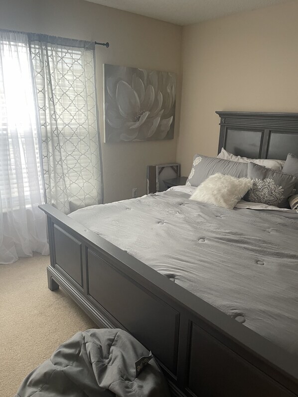 A bedroom with a large bed, a headboard, a nightstand, a TV, and a window with curtains.