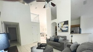 A spacious living room with a grey sofa, a coffee table, and a ceiling fan. A staircase leads to an upper level. - Wish Upon A Star 5 bed pool/jacuzzi spa heat included (Clermont)