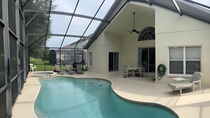 A covered swimming pool with a curved design, a ceiling fan, and a patio area with outdoor furniture. - Wish Upon A Star 5 bed pool/jacuzzi spa heat included (Clermont)