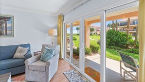A living room with a sofa, armchair, and a glass door leading to a balcony with a view of a golf course and buildings. - NEW LISTING!Stunning Sea Place Renovated -Oceanview 1st floor 2bd/bath (St. Augustine)