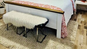 Un dormitorio con una cama, un banco, una lámpara colgante, un adorno de pared y un cuadro.