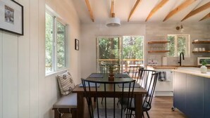 A dining area with a wooden table and chairs, a bench, and a view of the outdoors through large windows. - All New, 3 Bdrms, HOT TUB, near town and trails (Idyllwild-Pine Cove)