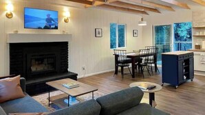 A living room with a fireplace, a television, and a dining area with chairs and a table. - All New, 3 Bdrms, HOT TUB, near town and trails (Idyllwild-Pine Cove)