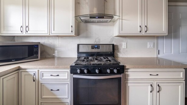 Una cucina con mobili bianchi, un forno a microonde in acciaio inossidabile e un piano cottura a gas.
