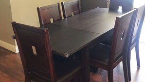 Un'area pranzo con tavolo e sedie in legno scuro abbinate, un quadro al muro e un frigorifero sullo sfondo.
