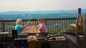 A wooden deck with a table and chairs, overlooking a scenic landscape with mountains and a bridge. - Relaxing Wintergreen Chalet (Wintergreen Resort)