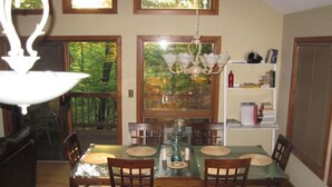 A dining area with a glass-top table, wooden chairs, and a chandelier. - Relaxing Wintergreen Chalet (Wintergreen Resort)