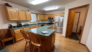 A kitchen with wooden cabinets, a central island with chairs, a microwave, stove, and refrigerator. - Golf Course, Close to YNP, Groceries, Restaurants (Island Park)