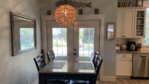 A dining area with a table and chairs, a hanging light fixture, and a view through the door. - Funky coconut luxury apartment (Dunedin)