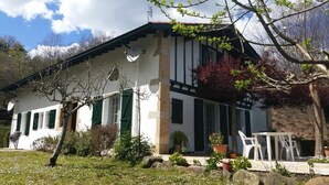 A white building with green shutters, a stone pillar, and a small patio area with potted plants and a white table. - GALARDIA - SARE - Gîte (SARE)