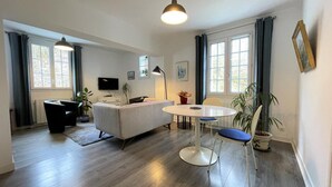 A modern living room with a sofa, a dining table, and chairs. There is a TV mounted on the wall, a lamp, and a potted plant. - GALARDIA - SARE - Gîte (SARE)