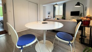 A modern living room with a round white table, two blue cushioned chairs, a sofa, a TV, and a red bowl on a side table. - GALARDIA - SARE - Gîte (SARE)
