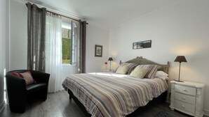 A bedroom with a large bed, a chair, a bedside table, and a nightstand. - GALARDIA - SARE - Gîte (SARE)