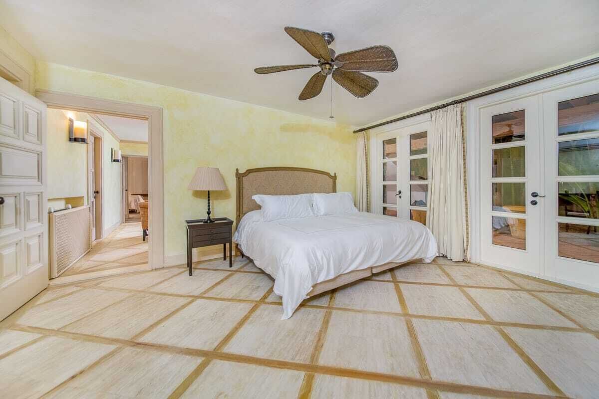 Une chambre à coucher avec un lit, une table de chevet, un ventilateur de plafond et une vue sur l’extérieur, visible à travers une porte vitrée.