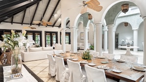 Une salle à manger spacieuse avec un haut plafond, des colonnes blanches et une grande table dressée pour un repas.