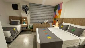 A hotel room with two beds, a desk, a chair, a fan, and a colorful abstract painting on the wall. - Hotel Medallo City (Medellín)