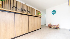 A reception area with a wooden reception desk, a potted plant, and a colorful sofa. - Hotel Medallo City (Medellín)