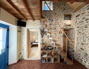 Een rustiek interieur met een stenen muur, een houten trap en een blauwe deur.