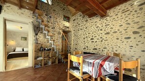 Une pièce rustique avec un mur en pierre, un escalier en bois, un lit, une table avec des chaises et une bibliothèque.